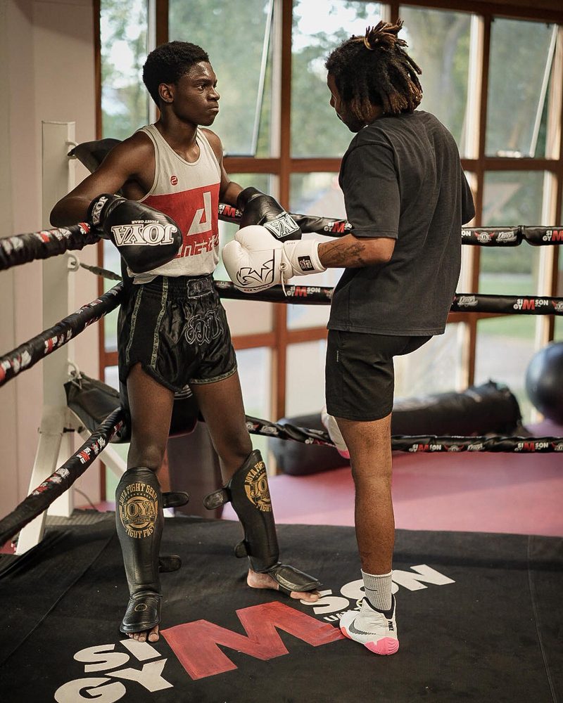 Een vechter met scheenbeschermers in de hoek van de ring, een trainer houdt een kickpad vast