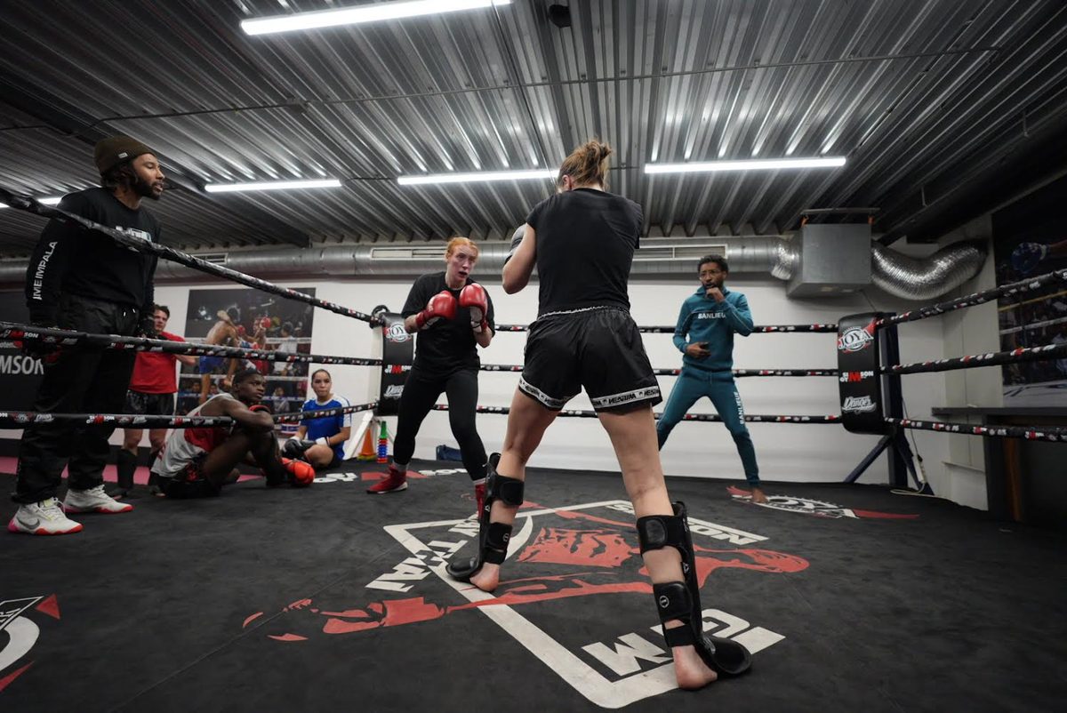 De trainingszaal van Simson Gym met een ring, sporters die trainen en trainers langs de touwen