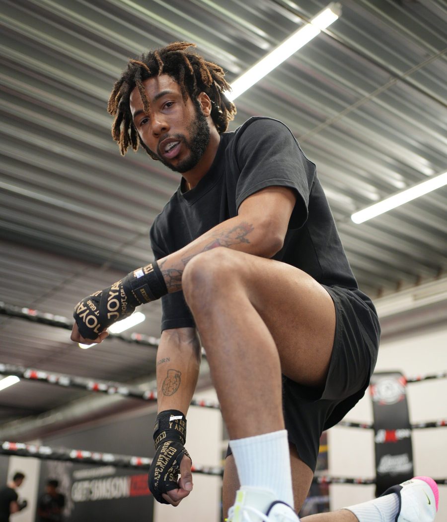 Een sporter in zwarte kleding zakt door zijn knie met bandages om zijn handen, in de ring van Simson Gym